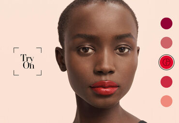 A close-up of a person with dark skin and short hair, showcasing bold red lips. The background is light, and there are color swatches of various lip shades on the right side. The text "Try On" is displayed in a stylish font.