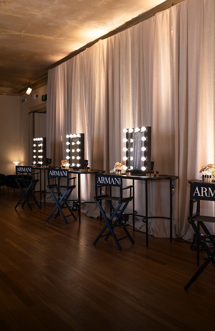 Eleganter Armani Beauty Veranstaltungsbereich mit Schminkspiegeln in warmem Gluhlampenlicht und minimalistischen schwarzen Hockern.