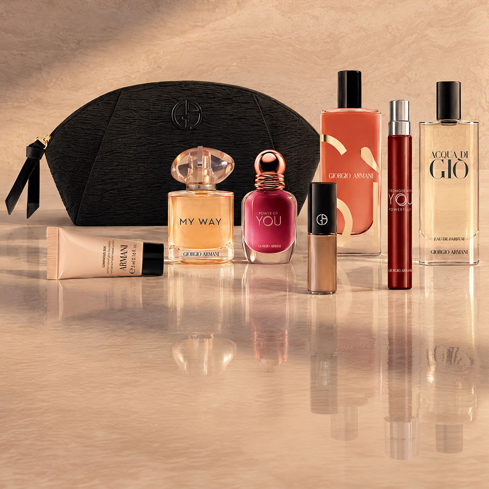 Eine schwarze Armani Beauty Kosmetiktasche mit Duften, Make-up und Pflegeprodukten vor beigem Hintergrund.
