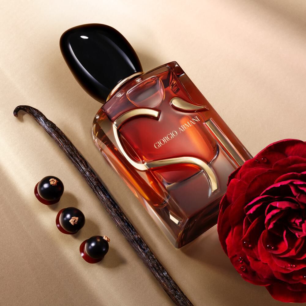 Giorgio Armani Si Parfum bottle lying next to a red rose, vanilla bean, and three blackcurrants.