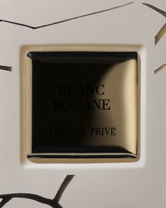 A white "Armani/Prive BLANC KOGANE" fragrance bottle with golden accents, overlaid with delicate white jasmine flowers, subtle gold lines, and an abstract human silhouette, evoking elegance and purity.