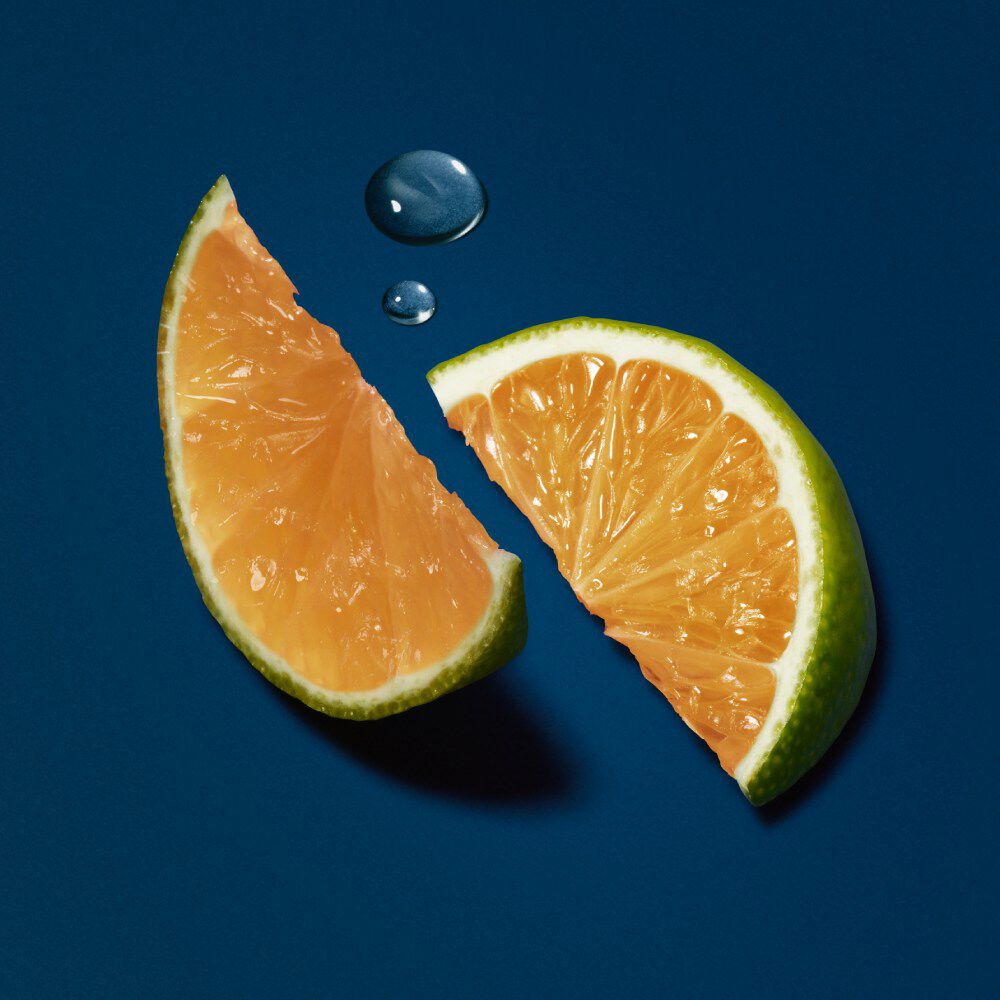 Zwei uberlagerte, frisch geschnittene Limettenhalften auf einem dunkelblauen Hintergrund mit Wassertropfen.