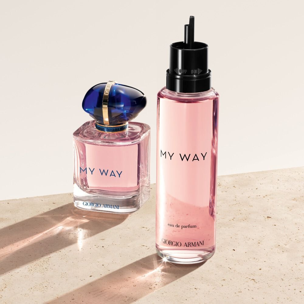 Eine Flasche und ein Nachfullflakon des Giorgio Armani My Way Eau de Parfum. Der Originalflakon, ein zartes Rosa mit blauer Kappe, steht neben seinem großeren, durchscheinenden rosa Gegenstuck zum Nachfullen. Sie stehen auf einer hellen, strukturierten Oberflache.