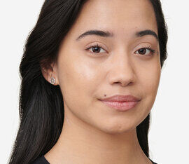 A close-up portrait of a young woman with straight black hair, wearing small stud earrings and a subtle smile. She has a natural look, with minimal makeup, and is facing the camera.