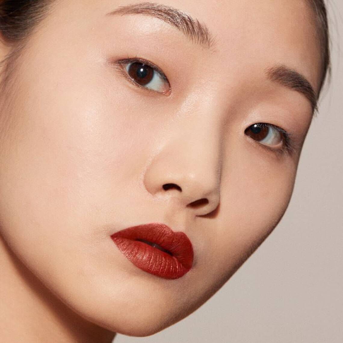 A close-up portrait of a woman with fair skin and dark hair, showcasing a natural makeup look with bold red lips and subtle eye makeup.