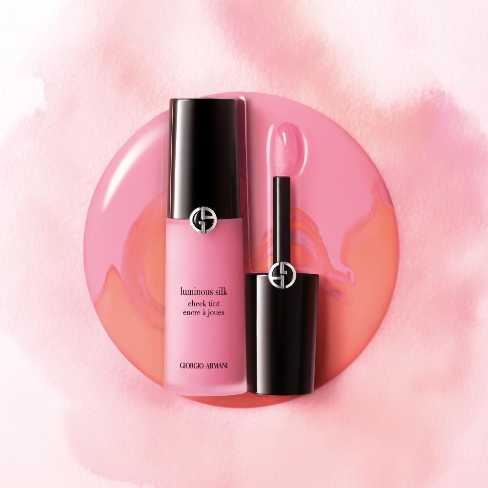 A bottle of Giorgio Armani Luminous Silk Check Tint in a vibrant pink shade, resting beside its applicator, set against a soft pink watercolor background.