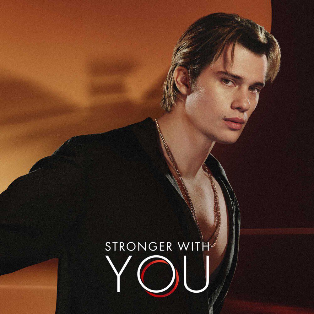 Nicholas Galitzine und das Stronger with You Logo, mit dem verschwommenen Emporio Armani Logo hinter ihm.