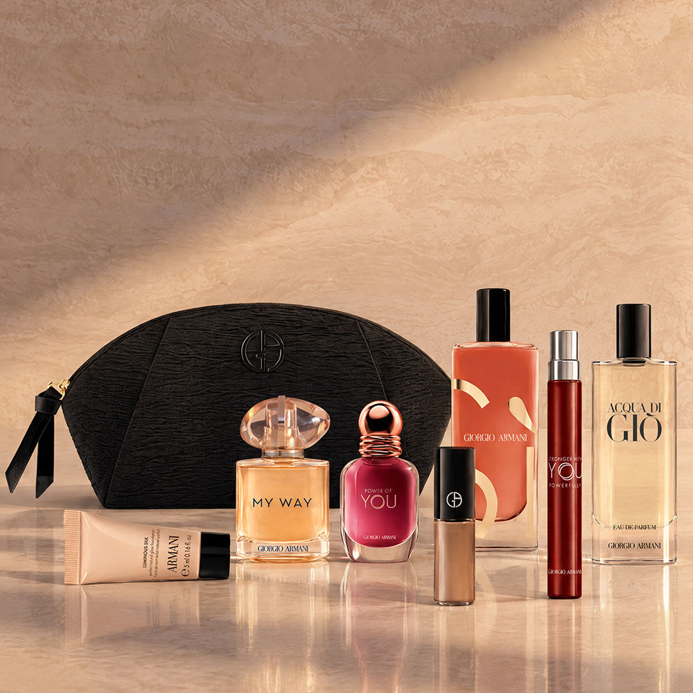 Eine schwarze Armani Beauty Kosmetiktasche mit Duften, Make-up und Pflegeprodukten vor beigem Hintergrund.