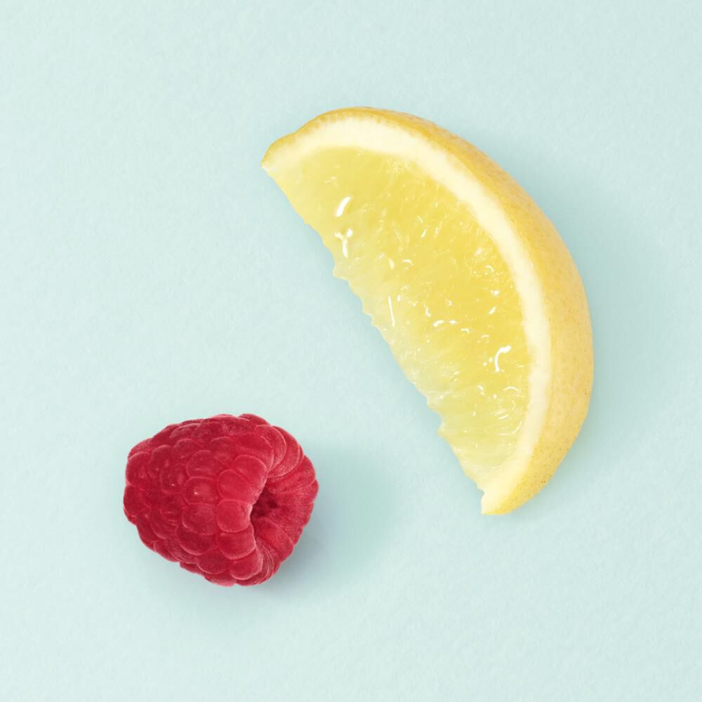 Eine Scheibe Zitrone und eine Himbeere auf hellblauem Hintergrund. Frische Fruchte, die fur einen Sommerlook stehen.
