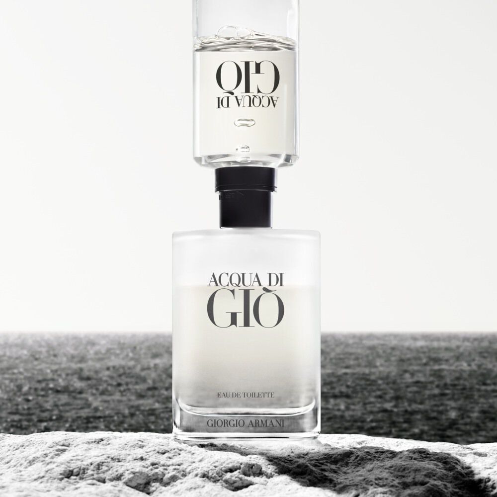 Ein Parfumflakon von Acqua di Gio steht auf einer Steinflache, mit dem Meer im Hintergrund und sanften Lichtverhaltnissen.