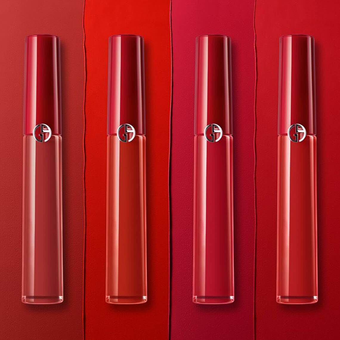 Four lip glosses are displayed in a gradient of red shades, from light to dark, against a matching background with color swatches. Each gloss features a sleek, transparent tube with a silver logo.