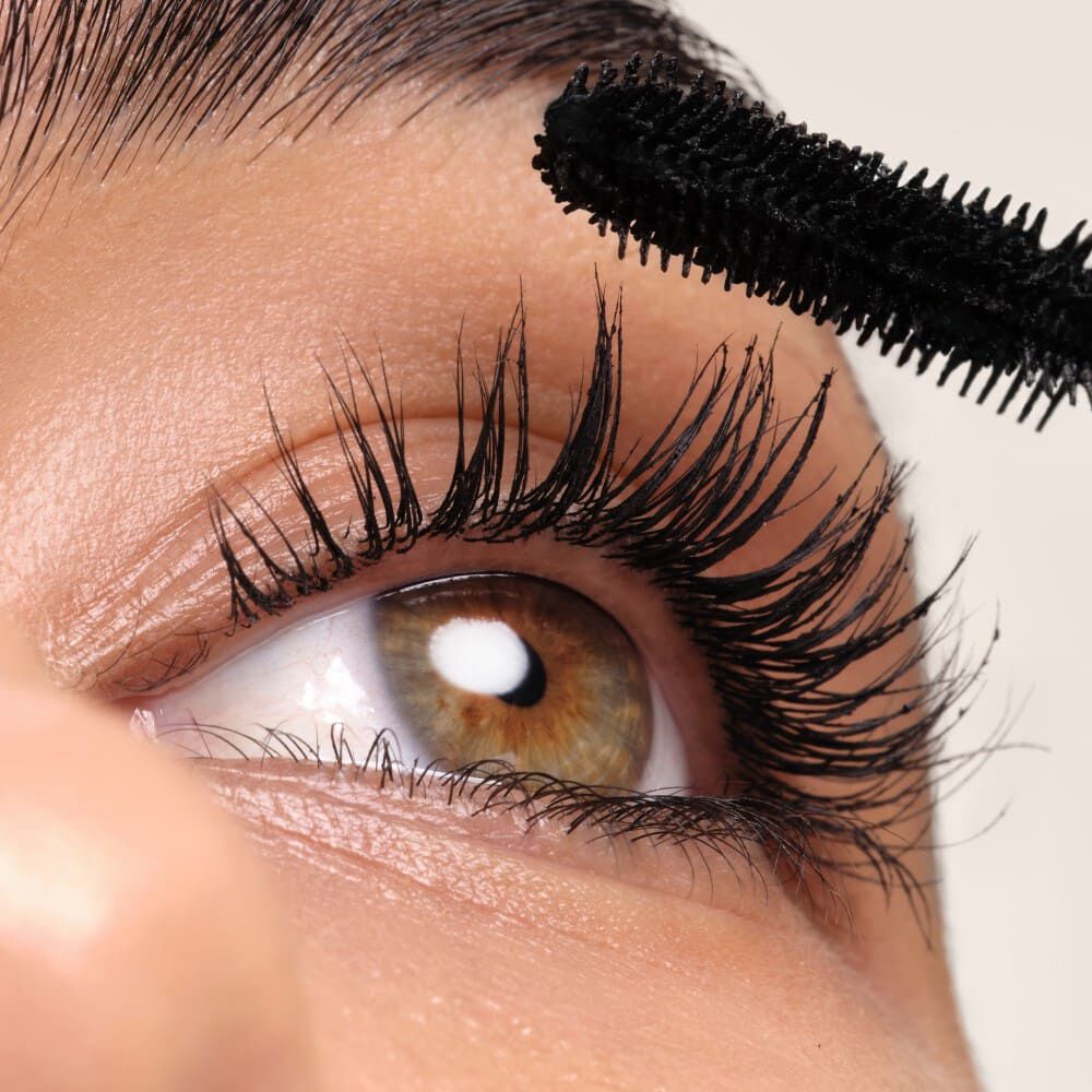 Nahaufnahme eines Auges mit langeren, dunkel getuschten Wimpern und einem Pinsel fur Wimperntusche.
