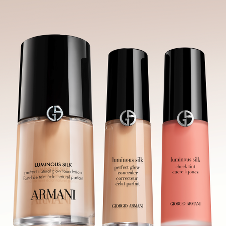 Die ikonische Luminous Silk Kollektion: Foundation, Concealer und Cheek Tint. Elegante Flakons mit schwarzen Verschlussen und silbernem Giorgio Armani-Logo vor sanftem Hintergrund verkorpern den legendaren, schwerelosen Glow von Armani Beauty.
