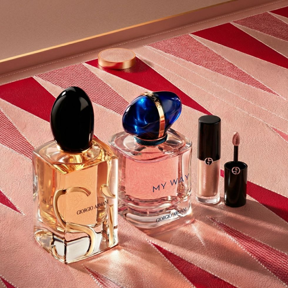 Eine luxuriose Auswahl an Armani-Ikonen: Die Dufte Si und My Way stehen neben einem eleganten Make-up-Essential. Der geometrische Hintergrund in Pink und Rot, inspiriert von der Couture, spiegelt zeitlose Schonheit und Handwerkskunst wider.