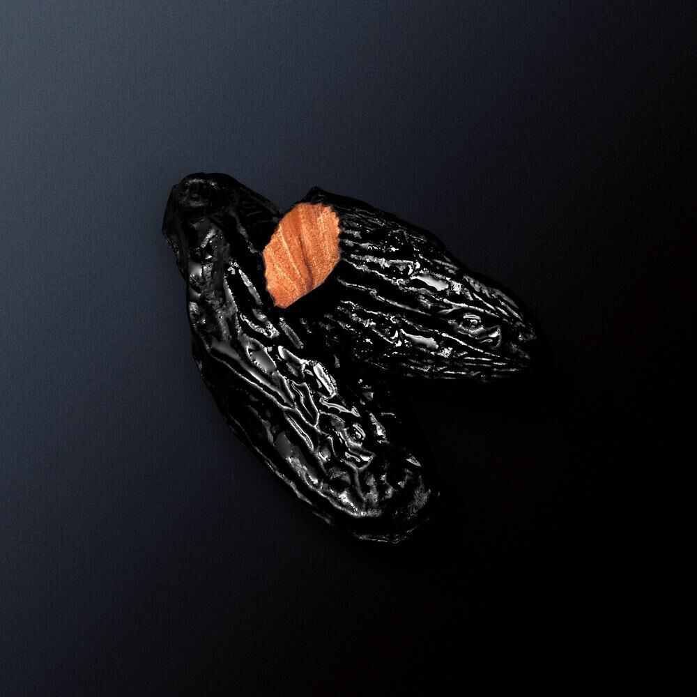 Zwei schwarze Tonkabohnen auf schwarzem Hintergrund, eine leicht geoffnet, die orangefarbene Innenseite sichtbar.