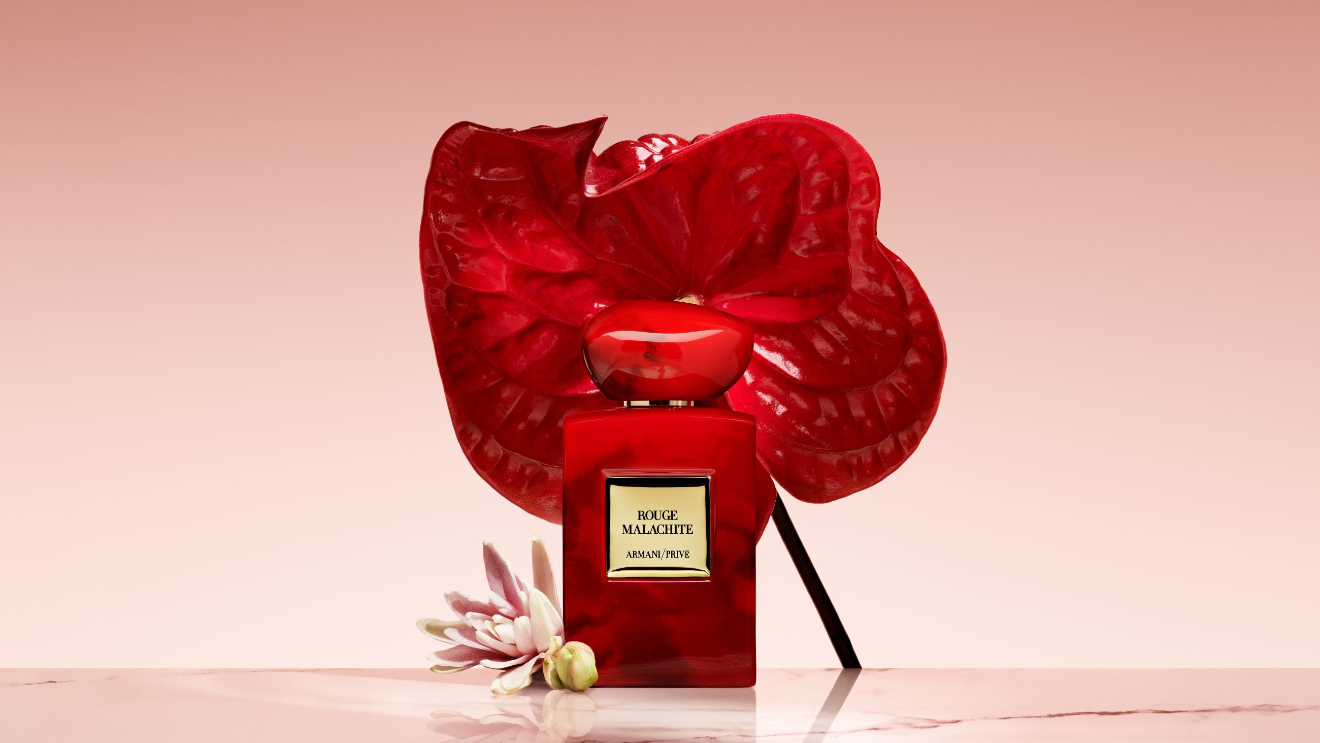 Armani/Prive Rouge Malachite Parfumflakon vor einer großen, leuchtend roten Blume.