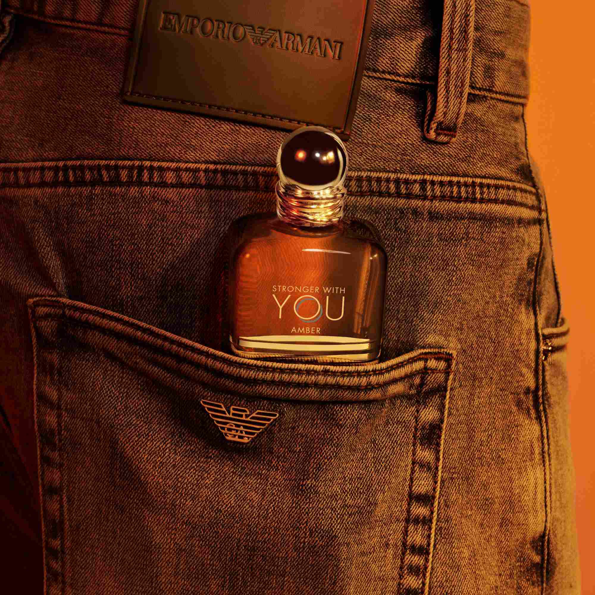 Eine Emporio Armani Stronger With You Amber Parfumflasche, die aus der Gesaßtasche einer Jeans ragt, mit einem dunklen Lederpatch daruber sichtbar