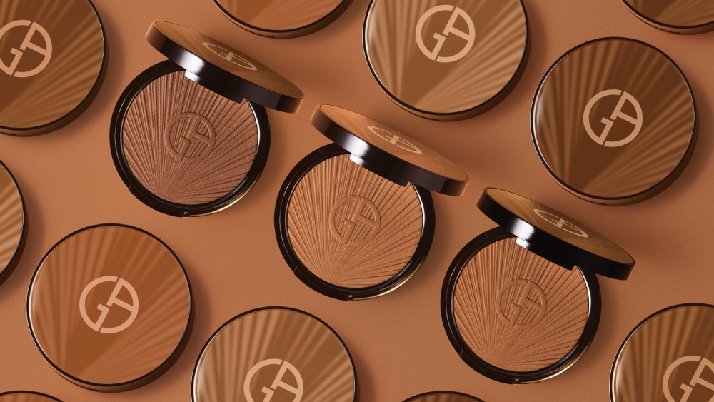Drei Make-up-Puder-Dosen von Armani in verschiedenen Brauntönen auf einem einfarbigen Hintergrund.