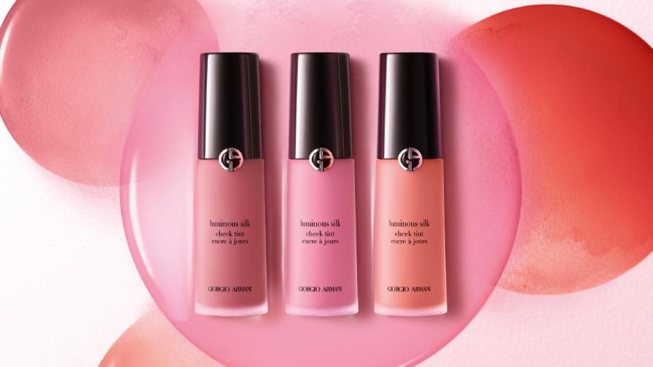 Drei Flaschen von Giorgio Armani Luminous Silk Blush in pinken und korallenfarbenen Tönen auf einem sanften Farbverlauf.