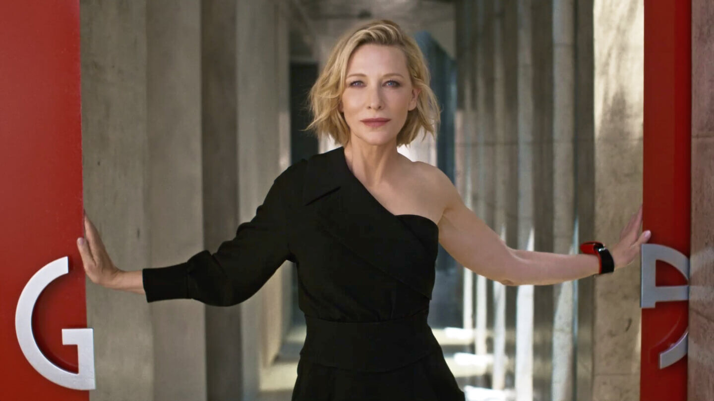 A stylish woman in a black dress stands confidently between two red pillars, embodying elegance and poise.