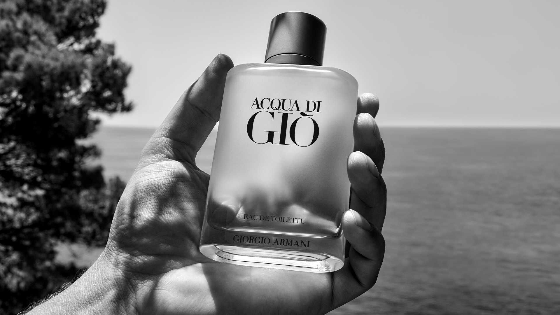 Ein Hand hält eine Flasche Acqua di Giò von Giorgio Armani vor einem Meereshorizont in Schwarz-Weiß.