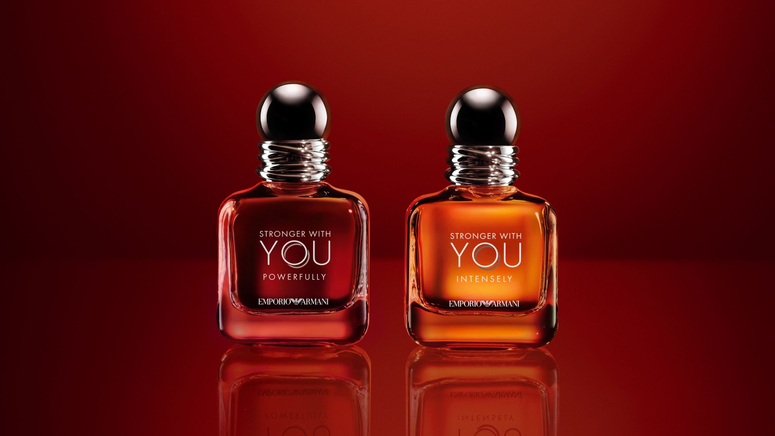 Zwei Flakons des Emporio Armani Parfüms „Stronger With You“ auf einem reflektierenden roten Hintergrund.