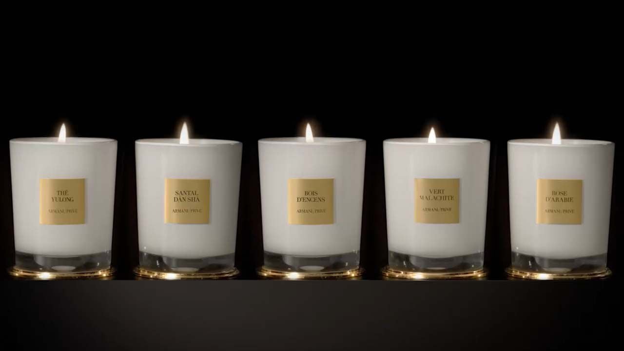 Fünf elegante Duftkerzen in Glasbehältern mit goldenen Etiketten auf schwarzem Hintergrund.